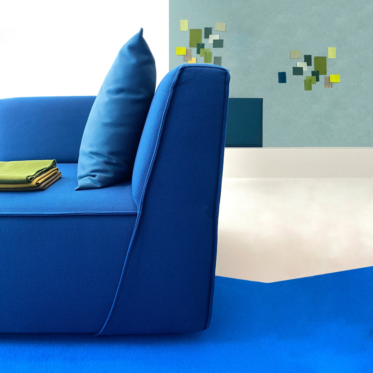 Seitliche Ansicht eines blauen Sofas mit Stoffmustern – im Hintergrund Wand mit Collage als Farbstudie