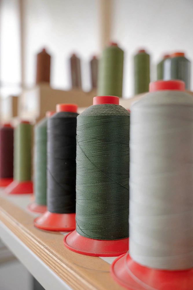 Close-up of various spools of thread in gray, dark green, and black a workshop that manufactures high-quality sofa covers.