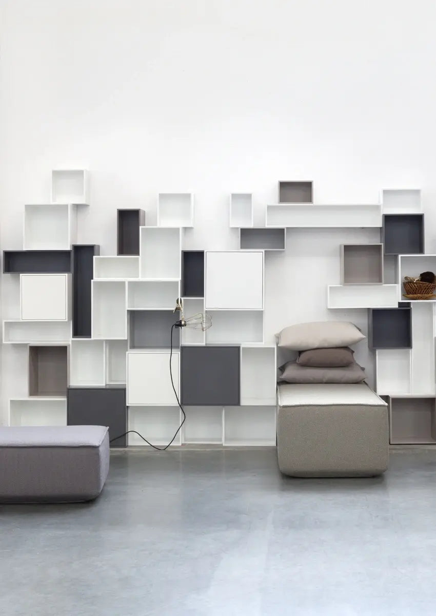 Modulares Regalsystem in Grau und Weiß an Wohnzimmerwand mit grauen Sofamodulen.