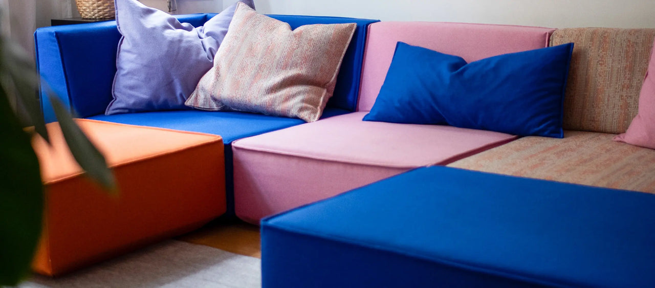 Nahaufnahme modulares Sofa in Blau, Orange und Rosa mit bunten Kissen im Wohnzimmer.