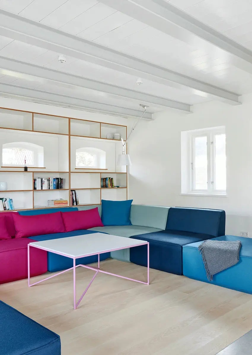 Modulares Sofa in Pink und Blau mit weißem Holzregal und rosa Couchtisch im Altbau.