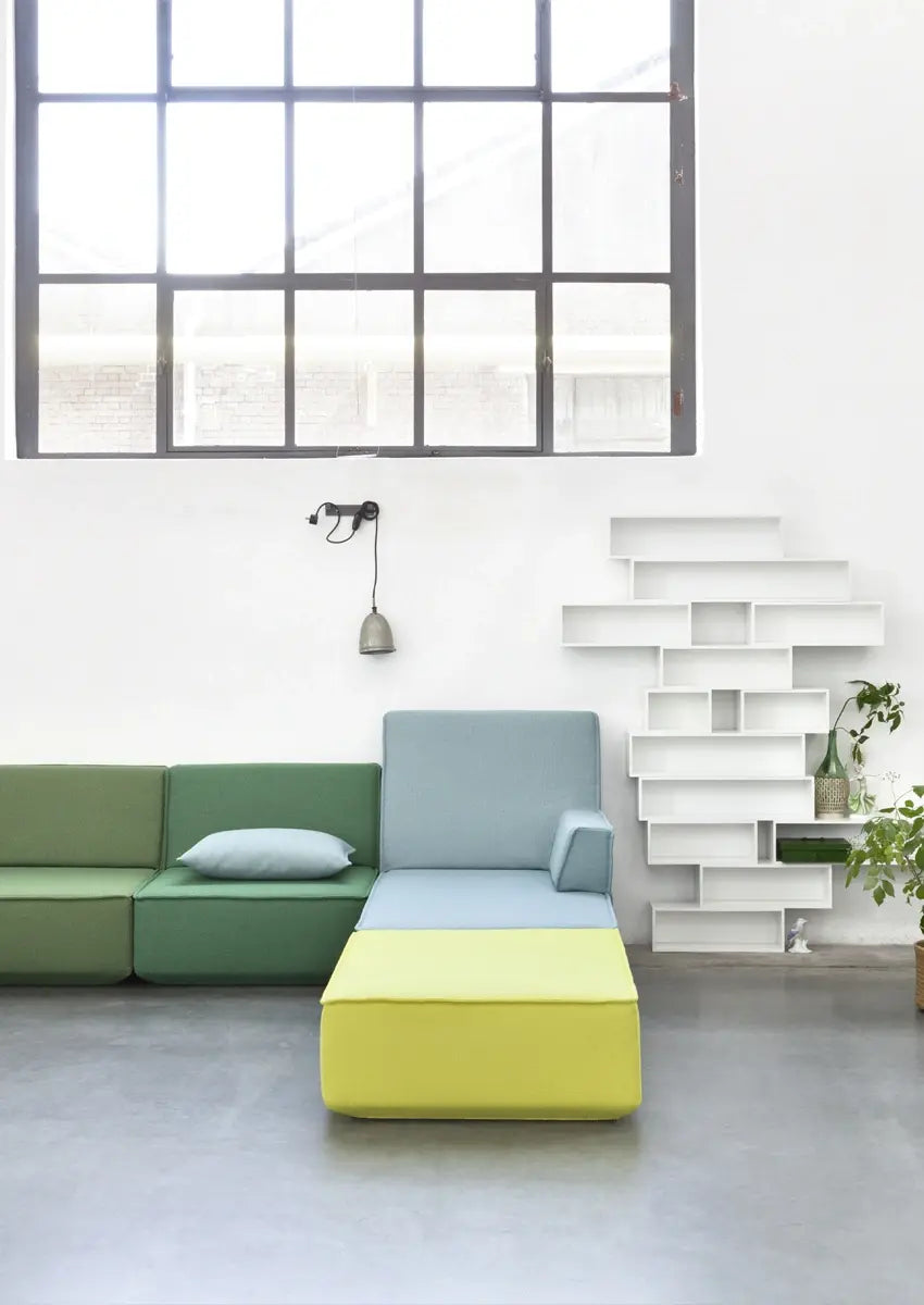 Modulares Sofa in Grün, Blau und Gelb mit weißem Regalsystem und Pflanzen.