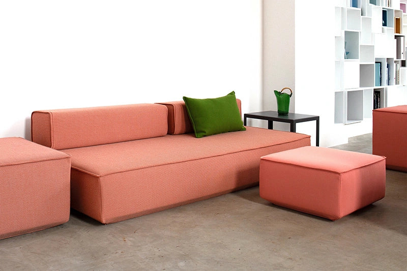 A coral-colored modular sleeper sofa with a matching ottoman and a green cushion, featuring modular backrests.