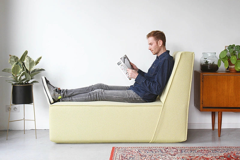 A man is sitting on a light yellow Cubit sofa module, reading, in a modern living room furnished withSideboard houseplants.
