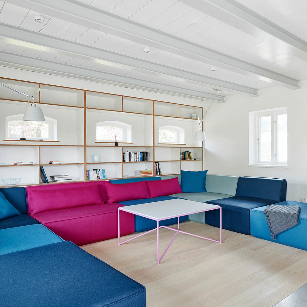 A modern living room featuring a colorful Cubit modular sofa arrangement in shades of blue and pink, set against a minimalist white wall shelf.
