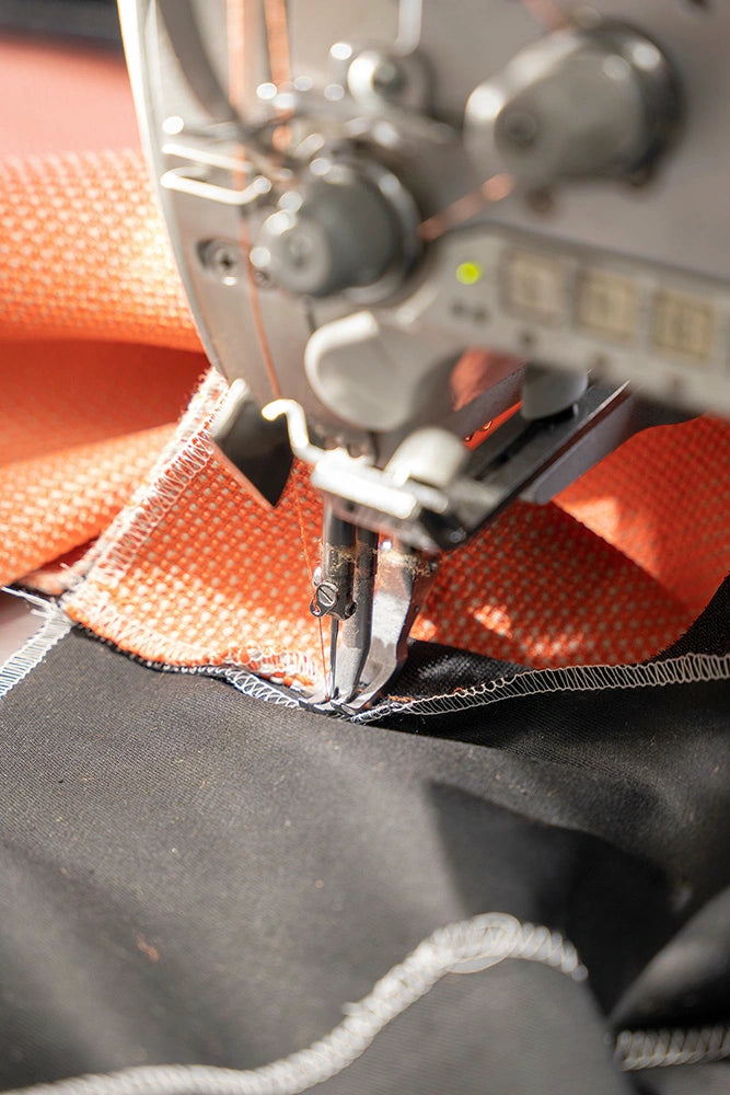 A close-up of an industrial sewing machine precisely sewing a sturdy orange upholstery fabric.