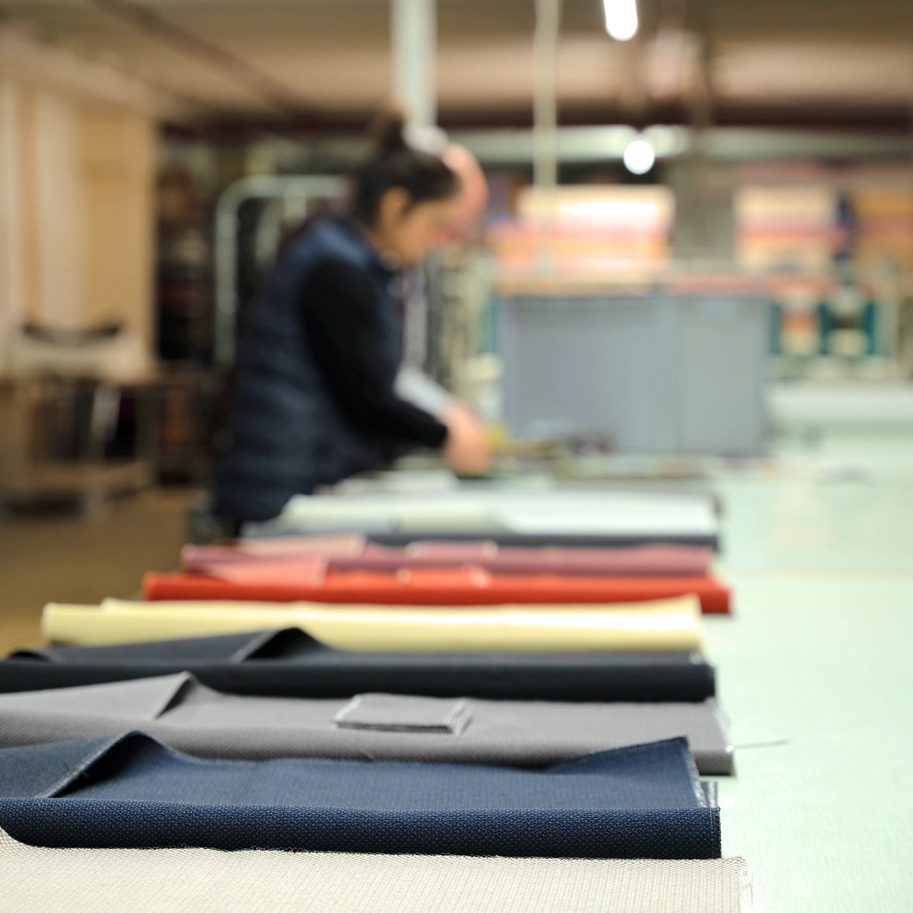 Zuschneiden von Stoffbahnen in der internen Näherei, im Vordergrund liegen sortierte Stoffmuster