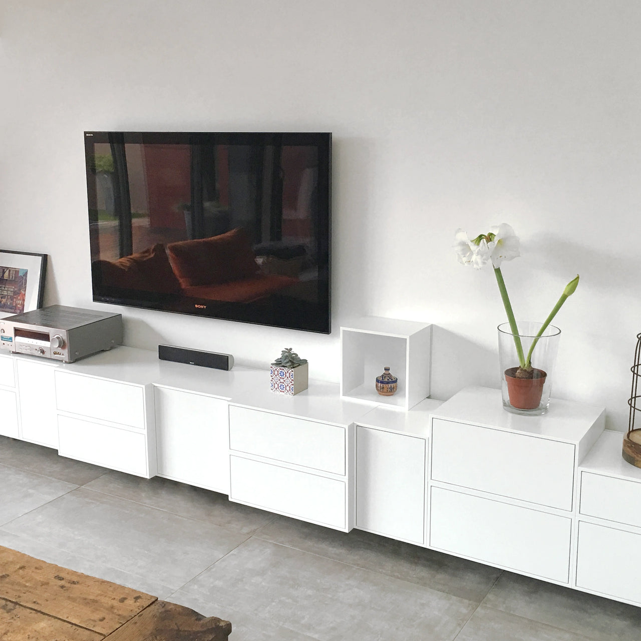 Modern white Shelving shelving with drawers and open modules, decorated with plants and ceramics, under a wall-mounted television