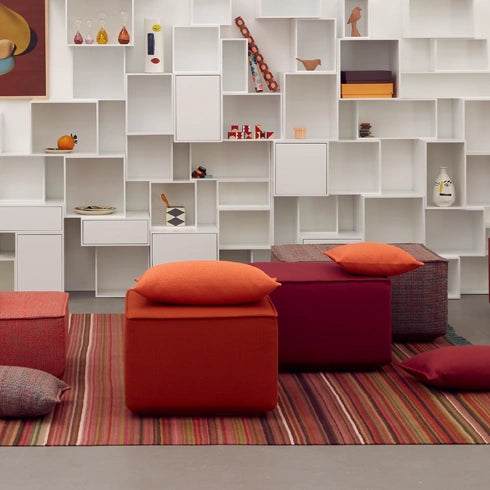 Pouffes in red and orange on a striped carpet, combined with modern wall bookshelf.