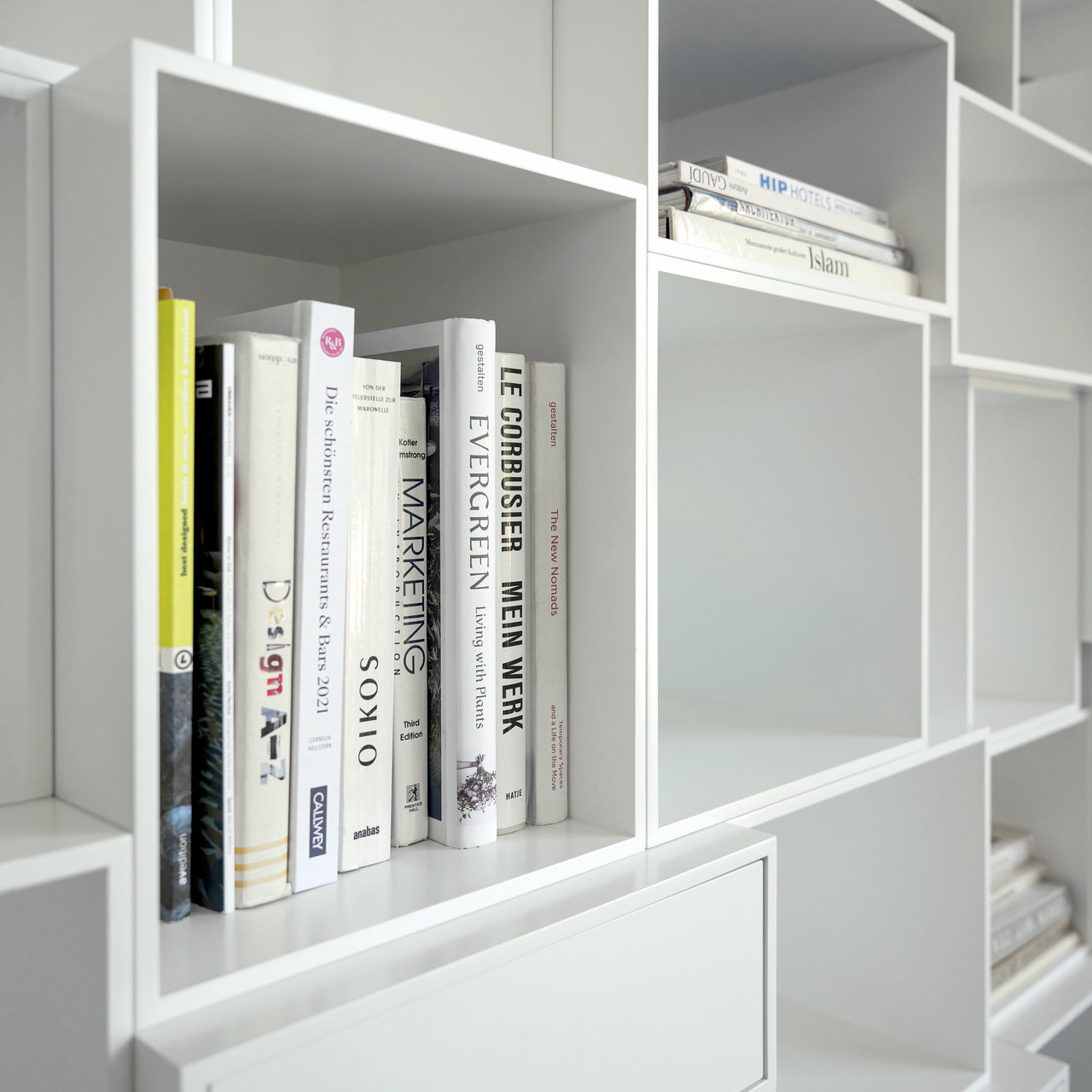 Gros plan sur un système d'étagères blanches avec des livres disposés verticalement et horizontalement