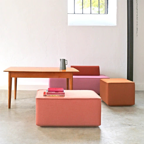 Bancs modulaires dans les tons rose, orange et rouge avec table en bois et fenêtre dans une pièce moderne et lumineuse avec sol en béton