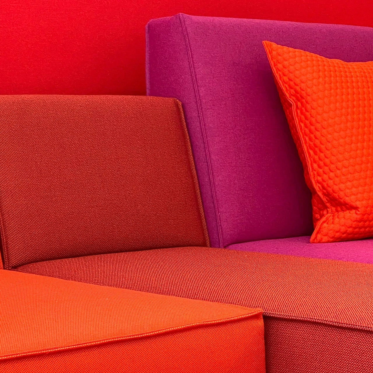 Gros plan sur des sièges modulaires recouverts d'un tissu rouge, orange et rose et d'un coussin en tissu 3D.