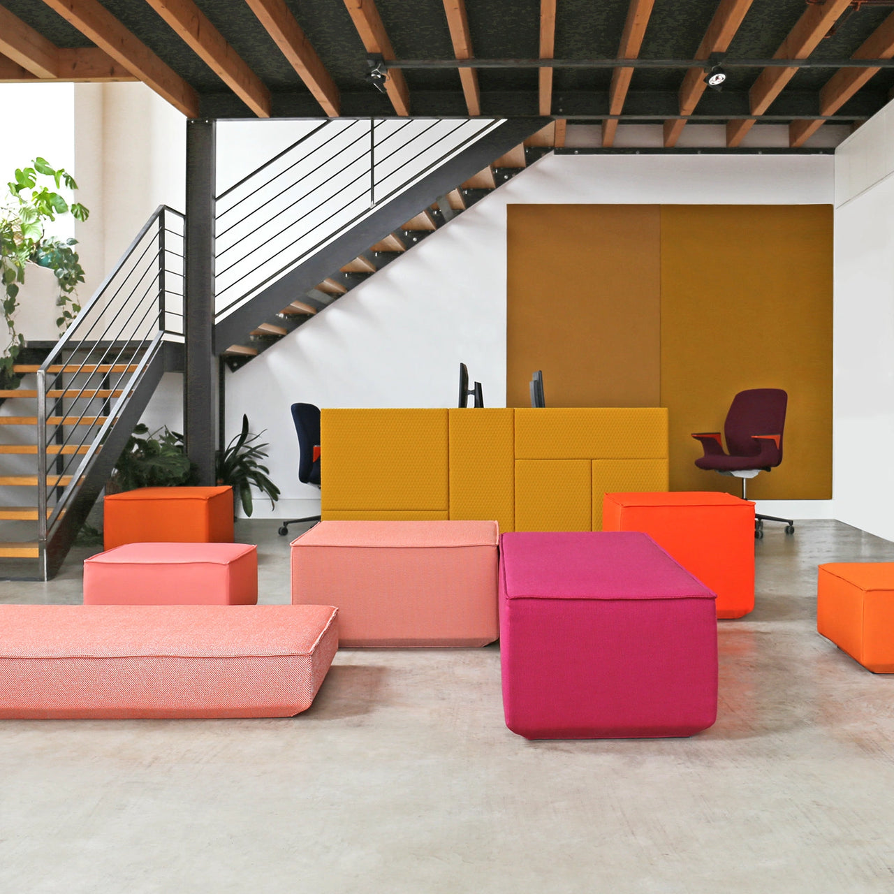 Meubles rembourrés modulaires colorés devant un comptoir acoustique jaune et une cloison acoustique dans un bureau moderne avec cage d'escalier ouverte.